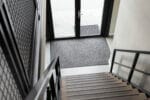 Praktijkvoorbeeld van de Ingresso Schoonloopmat. De mat is hier te zien in een thuissituatie, waarbij ook een trap en voordeur op de foto staan.