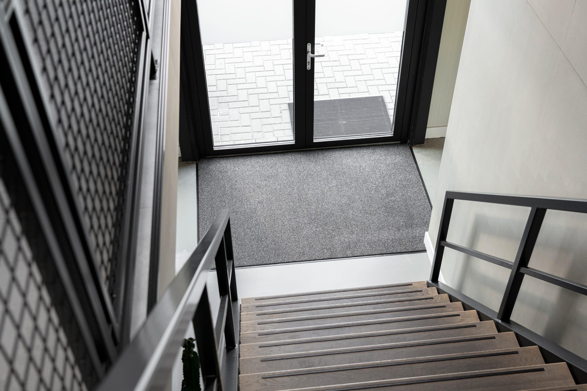 Praktijkvoorbeeld van de Ingresso Schoonloopmat. De mat is hier te zien in een thuissituatie, waarbij ook een trap en voordeur op de foto staan.